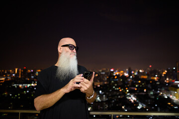 Portrait of mature man with gray beard outdoors at night using phone