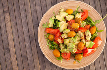 fresh salad of arugula, avocado, cherry tomatoes with olives on brown plate