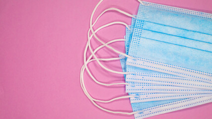 Typical 3-ply surgical masks on a pink background. 