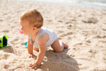 Small girl crawls on sand at beach near the sea
