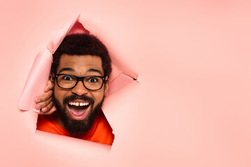 amazed and bearded african american man with open mouth on ripped pink background