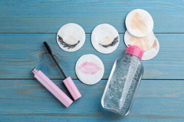Naklejka premium Dirty cotton pads, mascara and micellar cleansing water on blue wooden background, flat lay