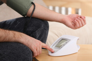 man checking blood pressure at wooden table indoors, closeup