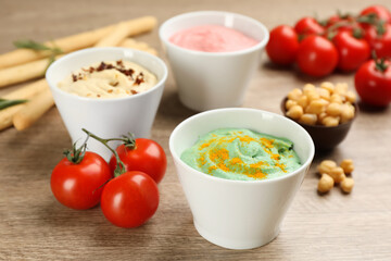 Different kinds of tasty hummus with ingredients on wooden table