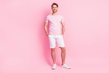 Photo of pretty funny young gentleman dressed casual t-shirt arms shorts pockets smiling isolated...