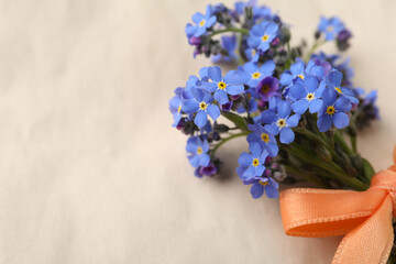 Beautiful blue forget-me-not flowers tied with ribbon on light background, closeup. Space for text