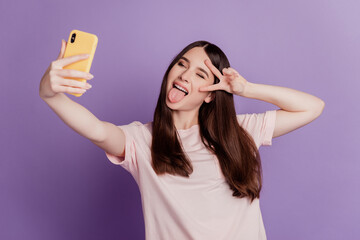 Naklejka premium Photo of cheerful cute young woman hold mobile phone shoot selfie show v-sign tongue