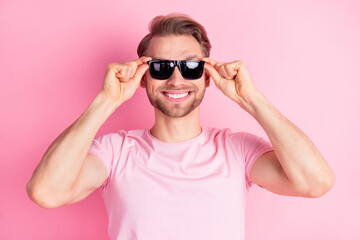 Photo of pretty charming young gentleman dressed casual t-shirt arms dark eyewear smiling isolated pink color background