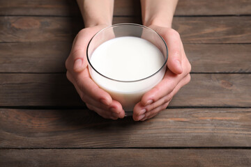 Woman holding glass of milk at wooden table, closeup