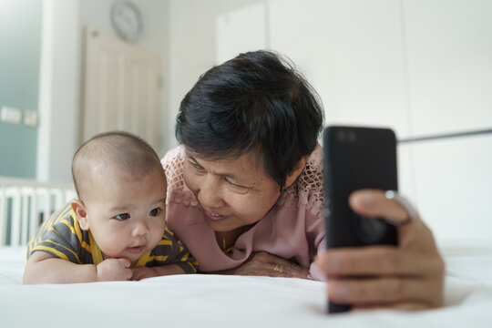 Happy Asian Grandmother and little baby boy or Grandchild playing and taking selfie photos with smartphone together