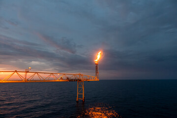 Fire on flare stack at oil and gas central processing platform sun set time while burning toxic and...