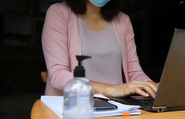 Closeup of woman' s hand working with notebook computer with bottle of alcohol gel. New normal working from home during COVID outbreak throughout the world.