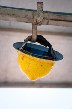An used yellow safety hardhat is hanging on the helmet railing rack's hook during the worker is taking a rest. Industrial PPE object photo. Selective focus.