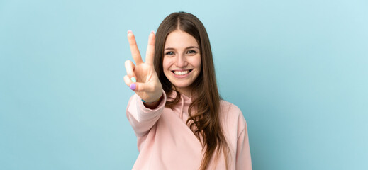Naklejka na ściany i meble Young caucasian woman isolated on blue background smiling and showing victory sign