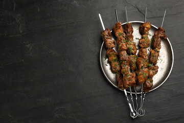 Metal skewers with delicious meat served on black table, top view. Space for text