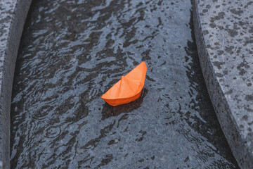 Launching an orange paper boat into the water on an artificial stream in the city. Children's fun on the water