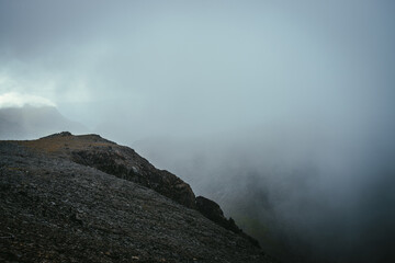Dark atmospheric landscape on edge of abyss in highlands. Dangerous mountains and abyss among low clouds. Danger mountain pass and sharp rocks in clouds. Dangerous cloudy rainy weather in mountains.