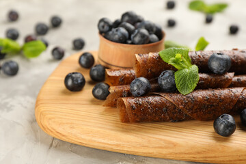 Delicious fruit leather rolls and blueberries on grey table, closeup