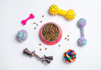 Different pet toys and feeding bowl on white background, top view