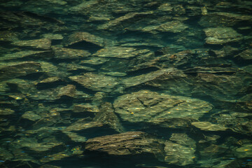 Meditative ripple of mountain lake. Beautiful relaxing background of stony bottom in turquoise transparent water of glacial lake in sunlight. Sunny backdrop with many stones in green clear water.