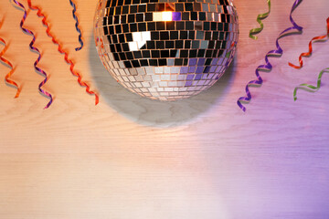 Shiny disco ball and serpentine streamers on white wooden background, flat lay. Space for text