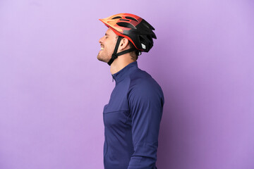 Young Brazilian cyclist man isolated on purple background laughing in lateral position