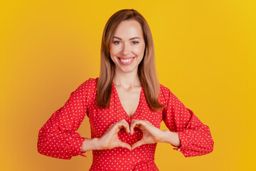 Portrait of charming lady formed a heart figure with the hands on yellow background