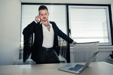 Uomo bianco con tatuaggi  vestito con una giacca con le frangechiama qualcuno con il telefono dal suo ufficio 