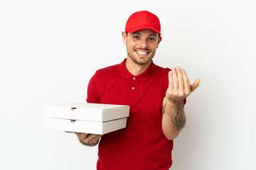 pizza delivery man with work uniform picking up pizza boxes over isolated  white wall inviting to come with hand. Happy that you came