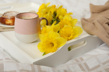 Bouquet of beautiful daffodils and coffee on bed, closeup