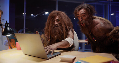 Primitive neanderthal people couple traveling through time working in contamporary office playing...