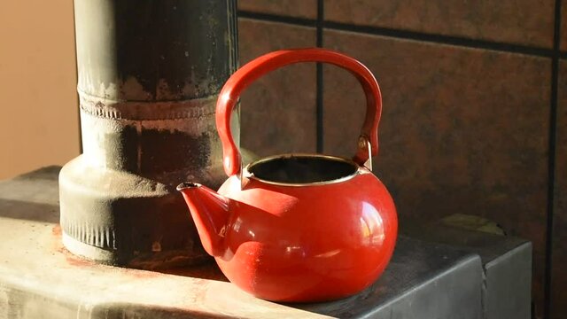 Red teapot steaming on old wood stove