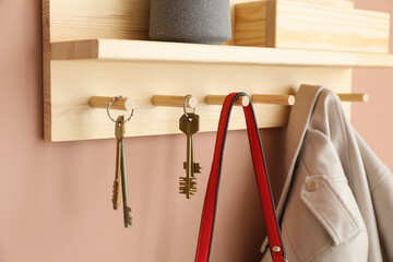 Wooden rack with hanging keys, jacket and purse on beige wall indoors