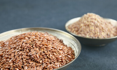 Flaxseed in a bowl with blurred ground linseed in background, selective focus.