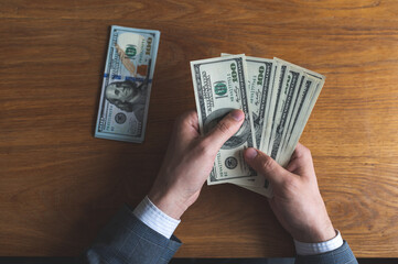 Male hands counting US Dollar bills or paying in cash on money background. Concept of investment,...
