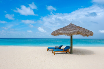 In the Maldives, two deck chairs with palm leaf sunshade on the beach of a private island