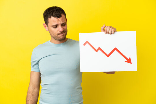 Brazilian man over isolated purple background holding a sign with a decreasing statistics arrow symbol with sad expression