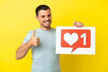 Brazilian man over isolated purple background holding a placard with Like icon with thumb up