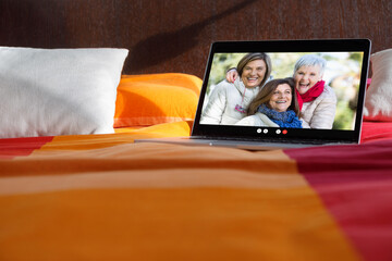Dettaglio di un computer portatile sul letto  nel cui schermo compaiono tre anziane amiche abbracciate  in remoto in videoconferenza  - obrazy, fototapety, plakaty