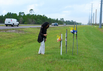 A grieving bereaved woman is placing flowers on crosses beside a busy road marking the location of where her friend was killed in a terrible drunk driver car wreck. - 430414946