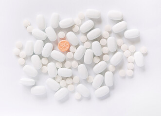 Fototapeta na wymiar White pills on a white background. One bright orange round pill accent. Oblong and round pills close-up. Healthcare and medicine.