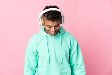 Young brazilian man isolated on pink background listening music