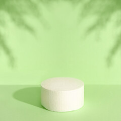 White round podium for cosmetic product against green background and shadow of leaves.