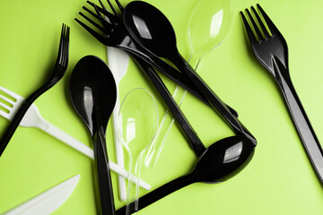 Forks, Spoons and Knives on green background. Plastic cutlery, ecology, environmental pollution by plastic, disposable tableware, waste recycling concept. Pattern, flat lay