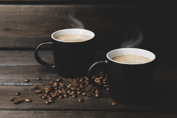 coffee with steam. two black cups and grains of coffee on a dark woody background