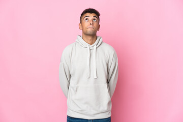 Young Brazilian man isolated on pink background and looking up