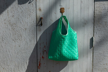 Green textured shopper bag hanging on the old grey door hanger.