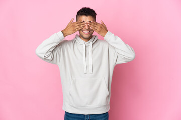 Young Brazilian man isolated on pink background covering eyes by hands and smiling