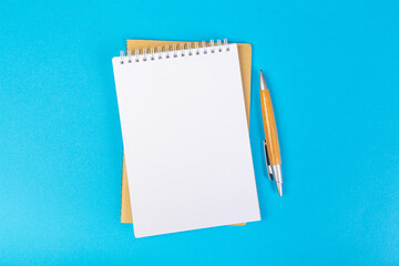 stack of school exercise books on blue background, spiral notepad with blank page and pen on table...