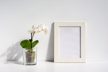 White photo frame with blooming orchid flower in transparent pot on a table
